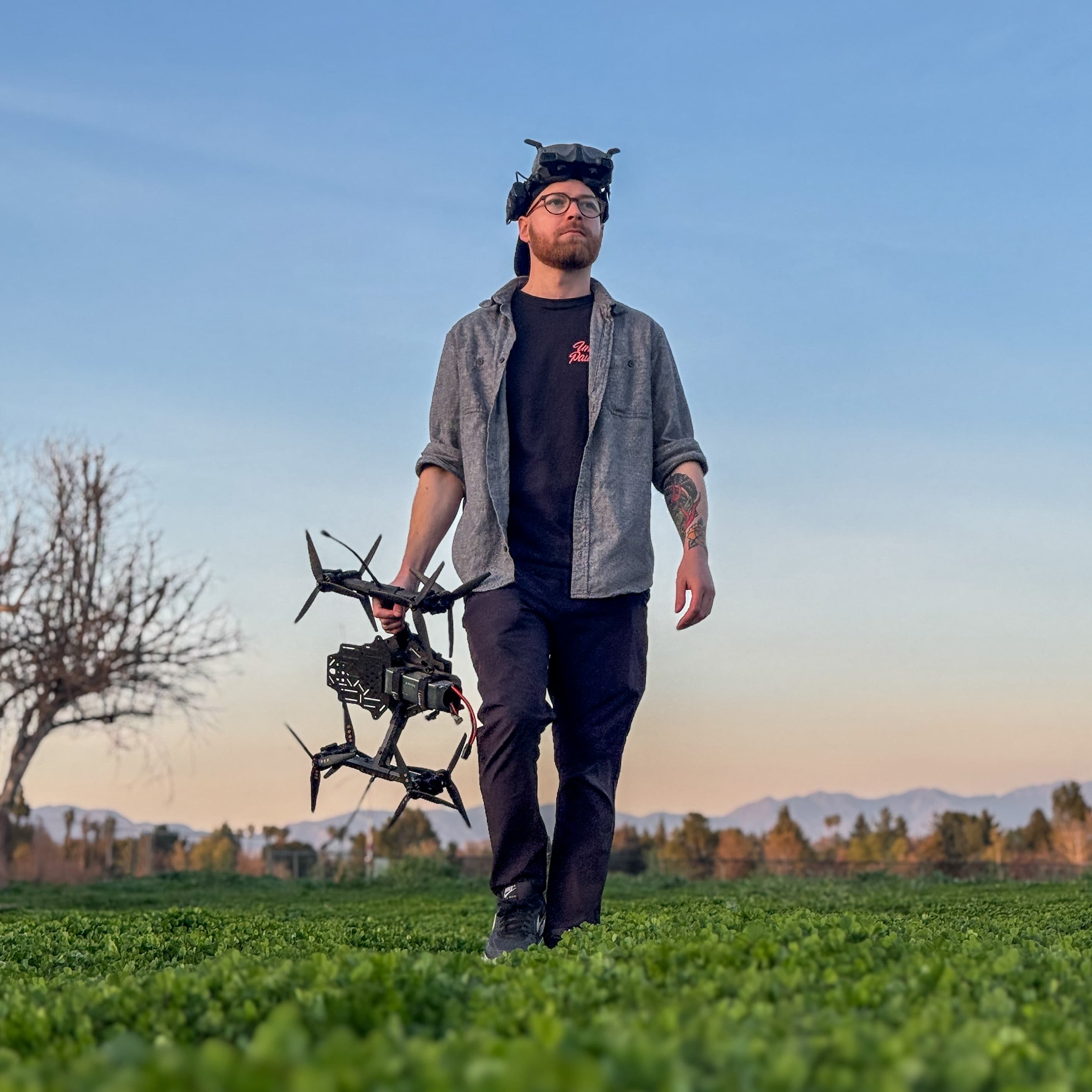 Zach Gilman, professional FPV drone pilot, standing in a field at sunset with drone equipment